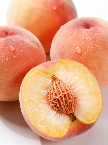 Целые и нарезанные персики на деревянном столе, рядом со стаканом персикового сока